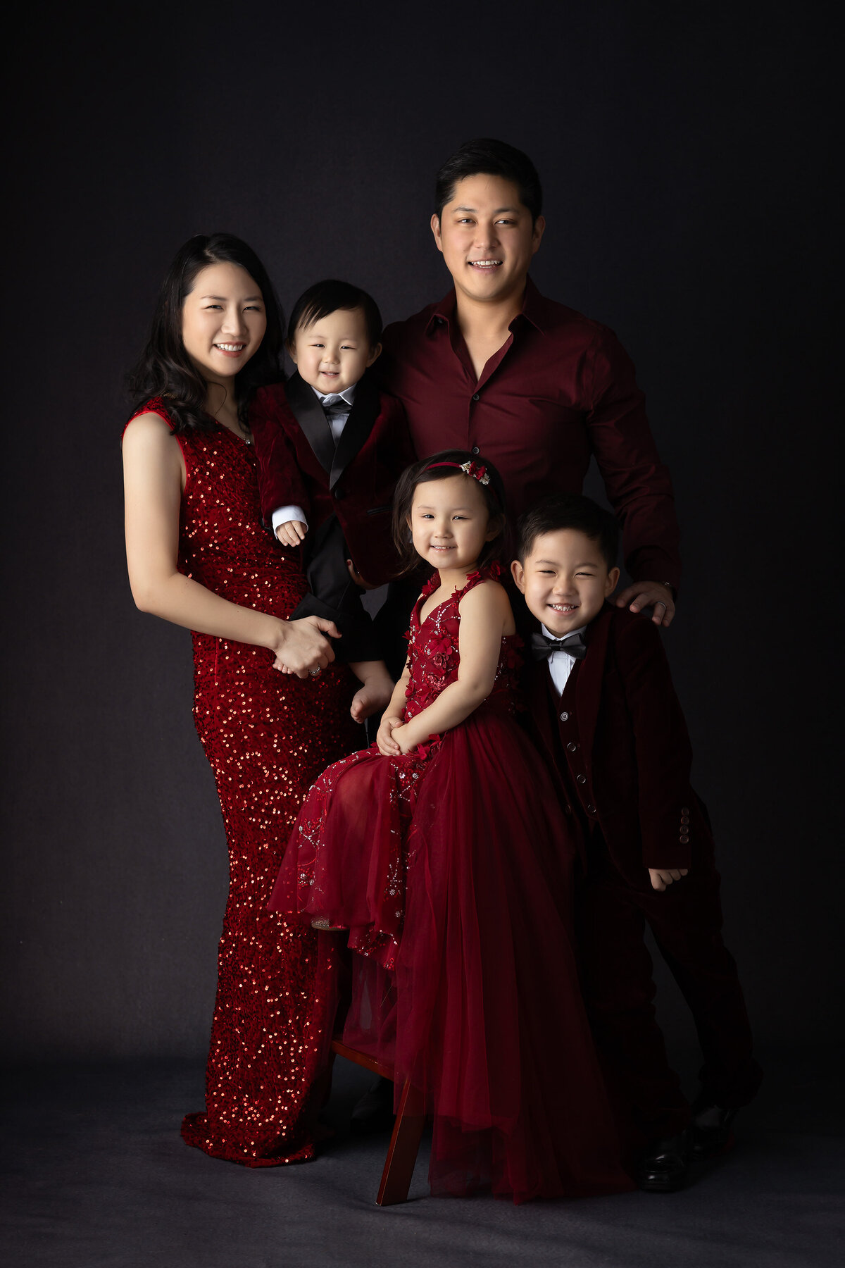 Dallas baby milestone photographer captures a stunning family portrait in matching red attire, with elegant poses and joyful smiles.
