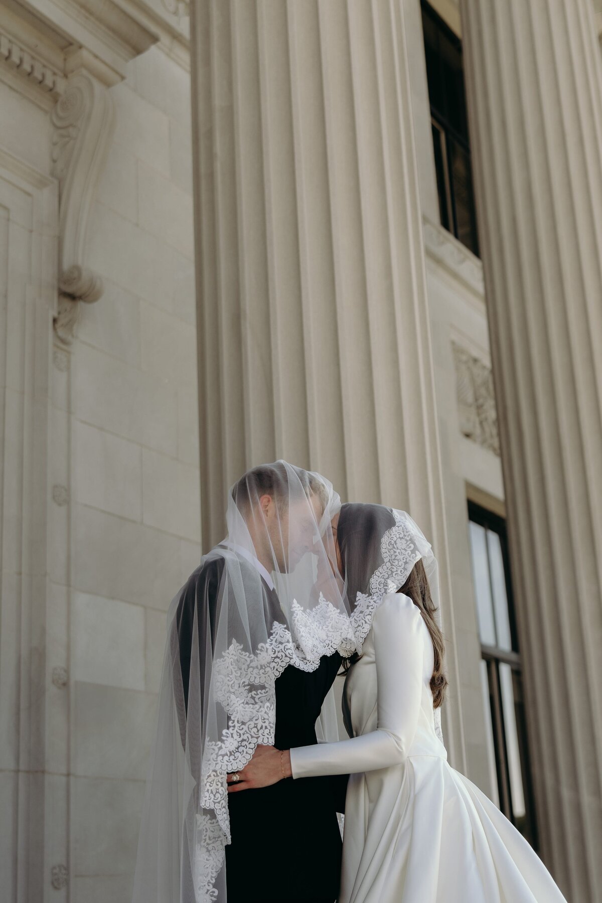 A classy wedding couple puts their faces in close as they share a kiss under the veil.