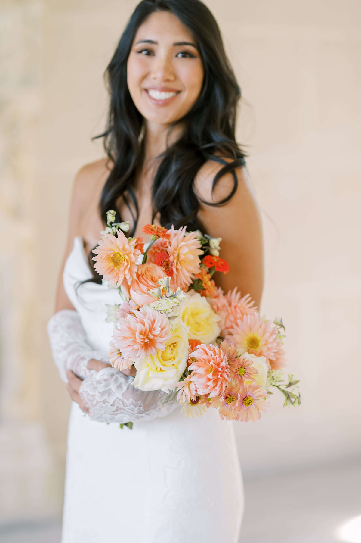 Bride smiling for a portrait while holding her peach colored bridal bouquet created by a DC wedding florist.