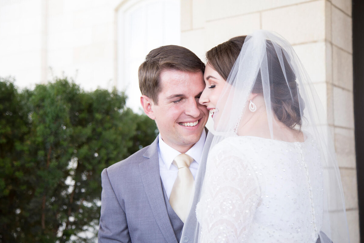 Bride in a veil laughing closely with groom in a gray suit