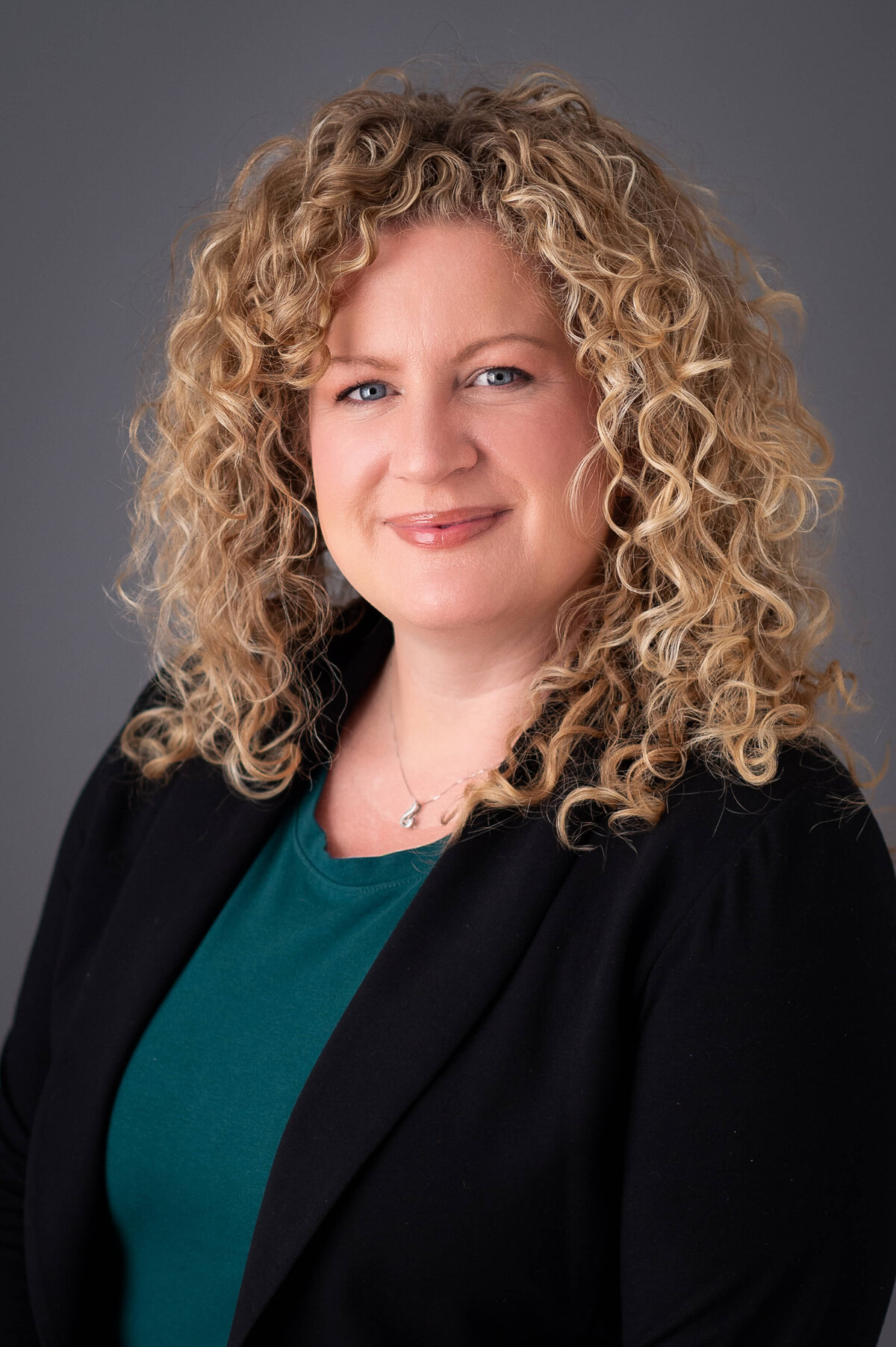a classic corporate headshot of a woman with blonde curly hair and green blouse.  Captured in-studio by Ottawa headshot photographer JEMMAN Photography