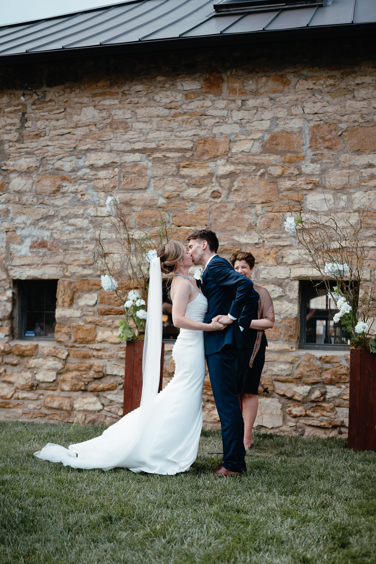 A bride and groom have their first kiss after their wedding ceremony  in front of a stone wall