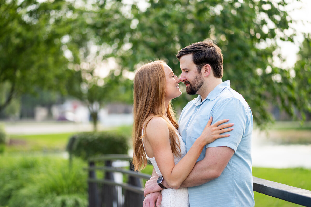 Engagment photoshoot couples nose to nose nuzzle as he pulls her in close while they are perched up on a bridge