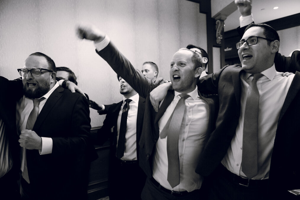 A black and white photo of men in suits cheering.