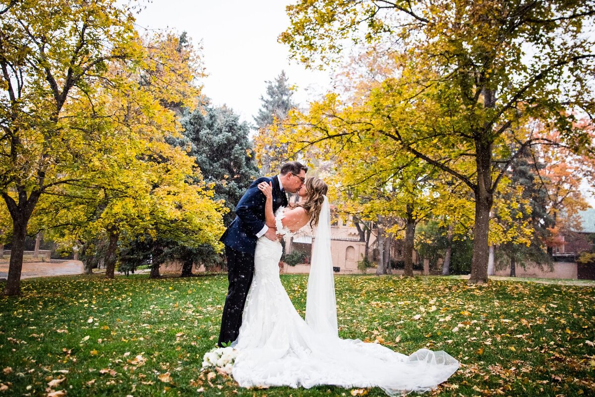 A groom dips his bride for a kiss with fall leaves around them.