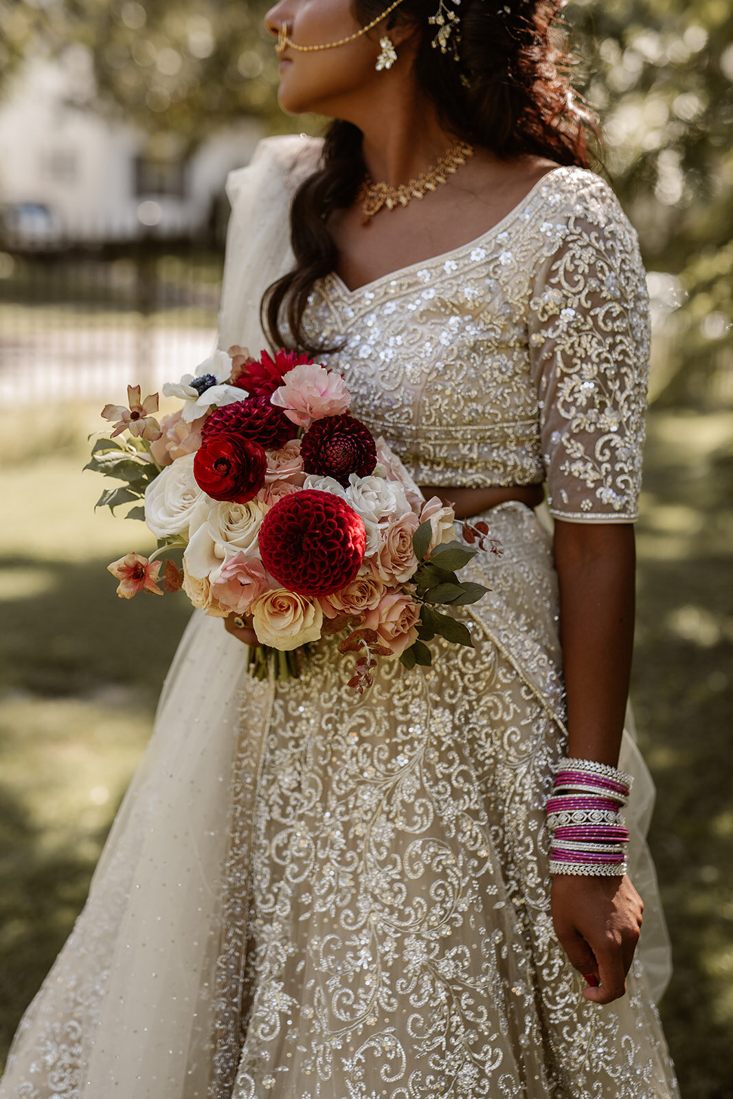 A close-up of the bride holding a stunning bouquet of deep red and blush florals, complementing her ornate bridal attire and traditional pink bangles.