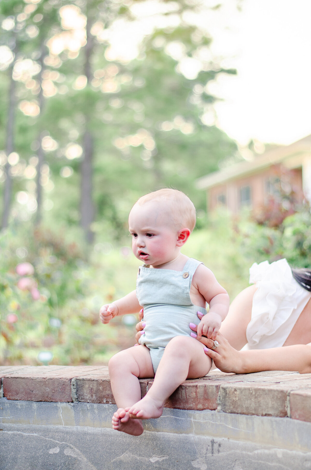 baby boy in mint romper sits on the edge of a fountain in a rose garden