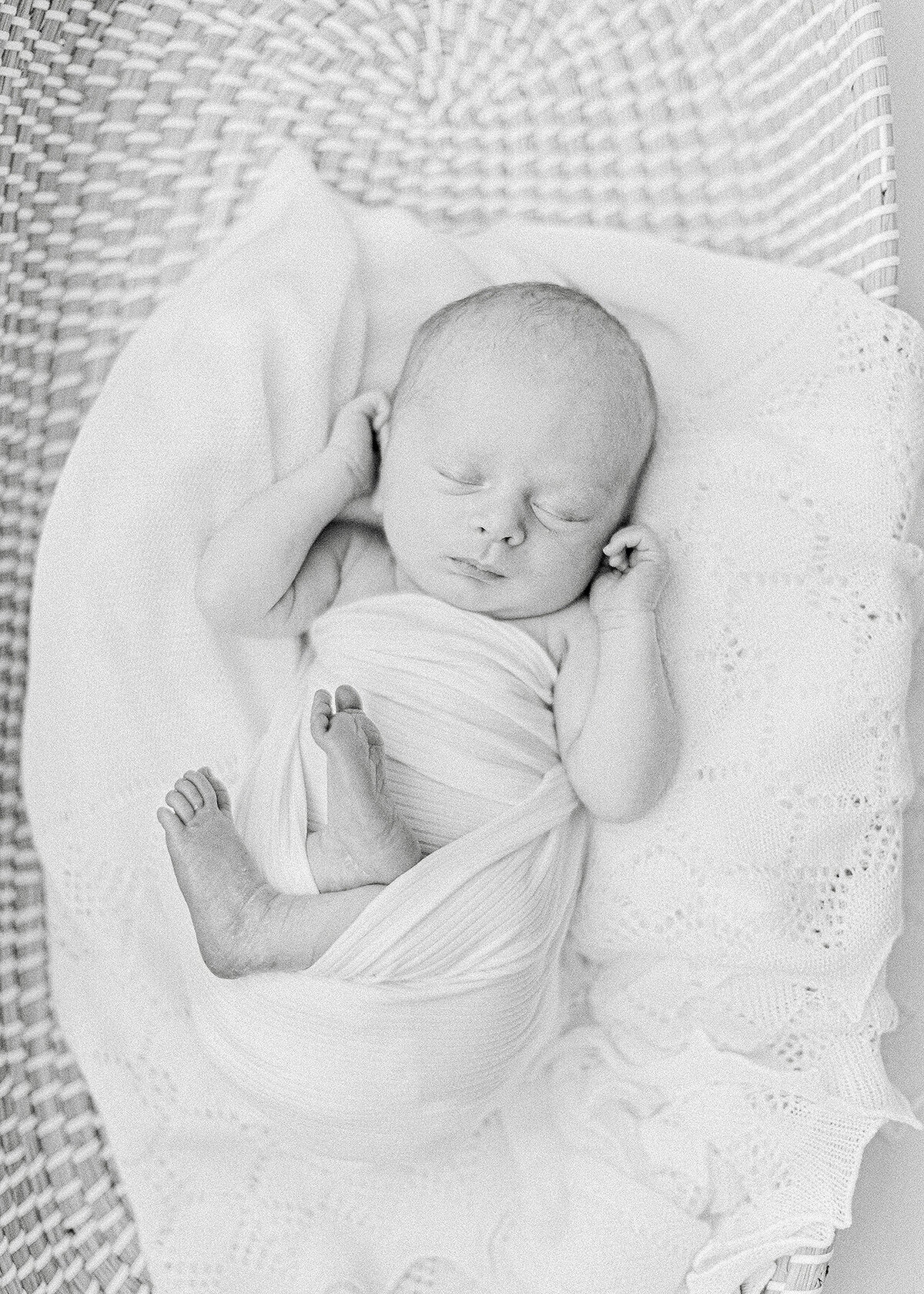 Black and white photo of a newborn baby boy laying down in a basket for his newborn session in a Dallas photography studio.