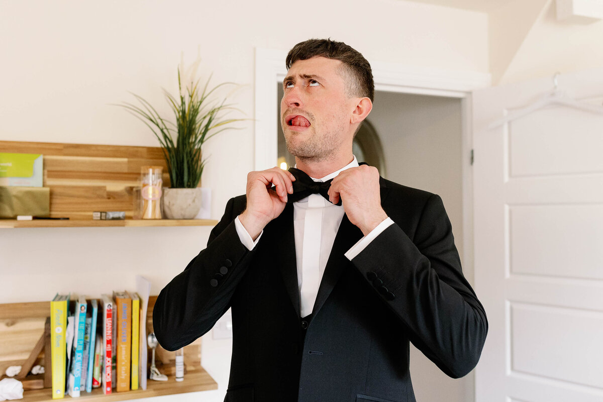 Groom pulling a silly face as he adjusts his bow tie at Wharfedale Grange