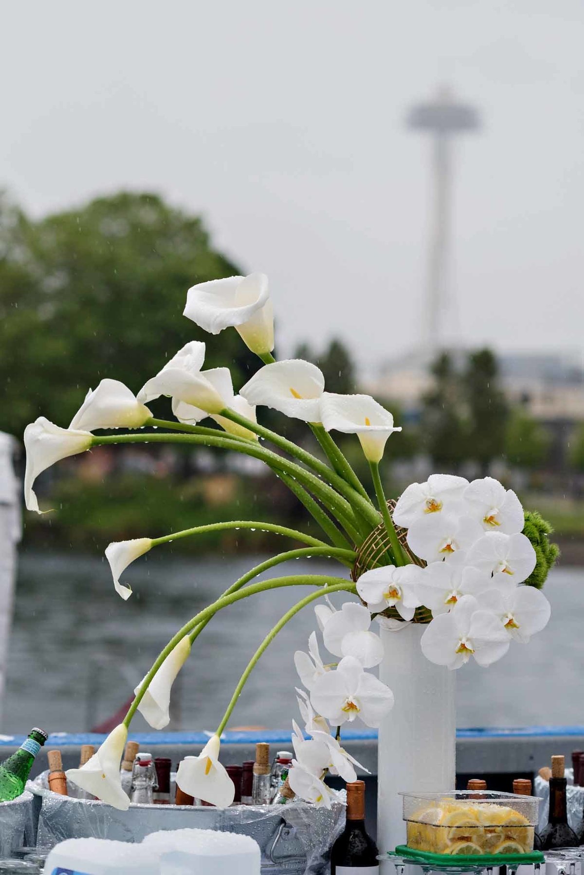 large arrangement of white calla lilies, white orchids, in tall white vase with Seattle space needle for large company party on a boat