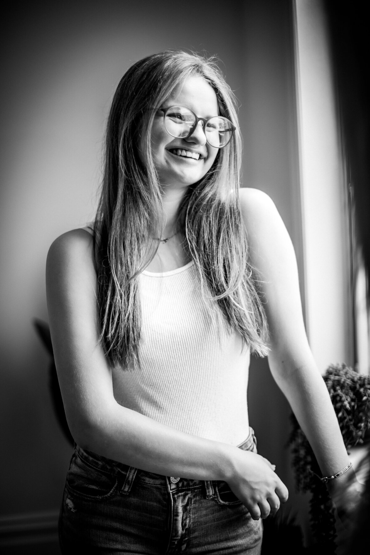 Striking black-and-white portrait of a girl in her mid teens wearing glasses as she smiles with window like lighting at the Pittsburgh photography studio