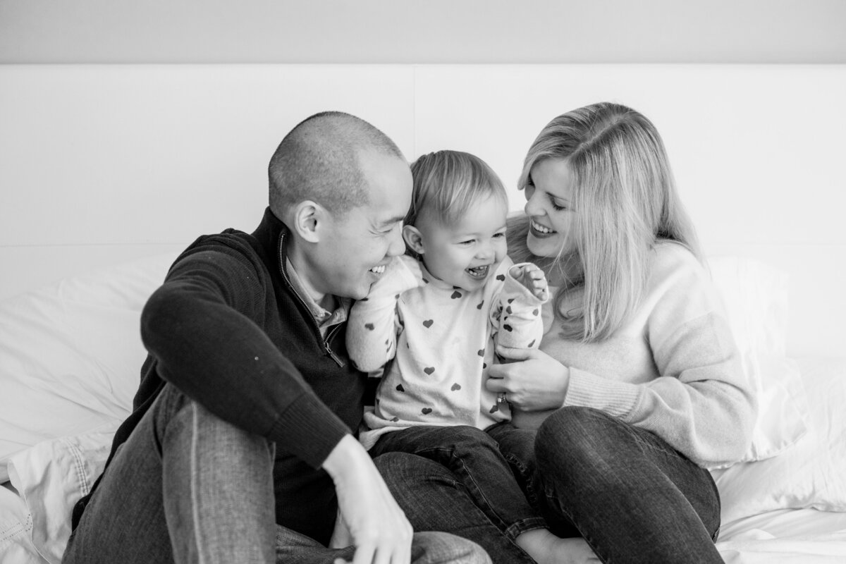 Family of Mom and Dad snuggling with toddler on bed