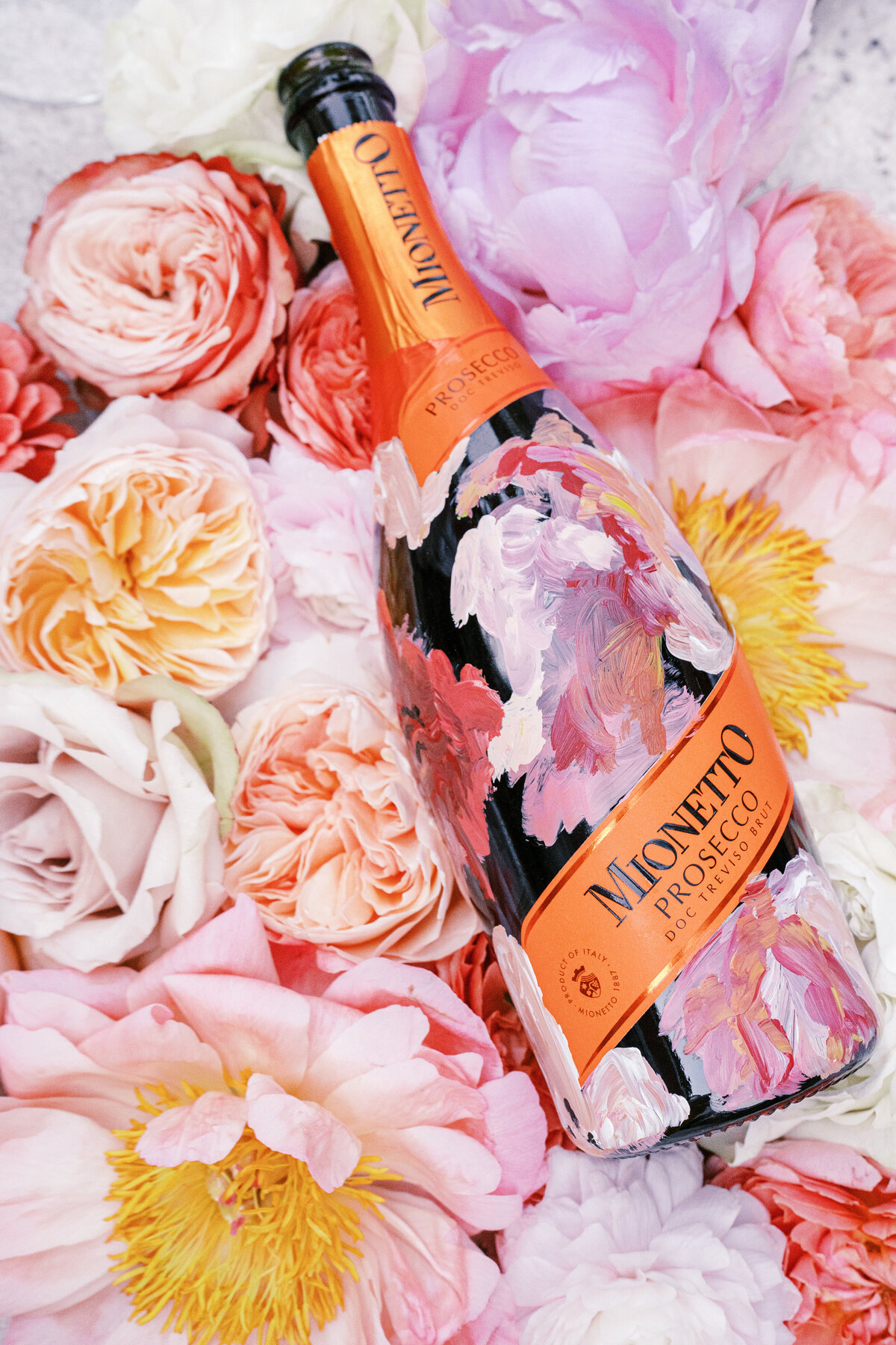 Hand painted Prosecco bottle in pinks surrounded by large colorful flowers for a Lake Como Italy wedding photographed by Lake Como Wedding photographer