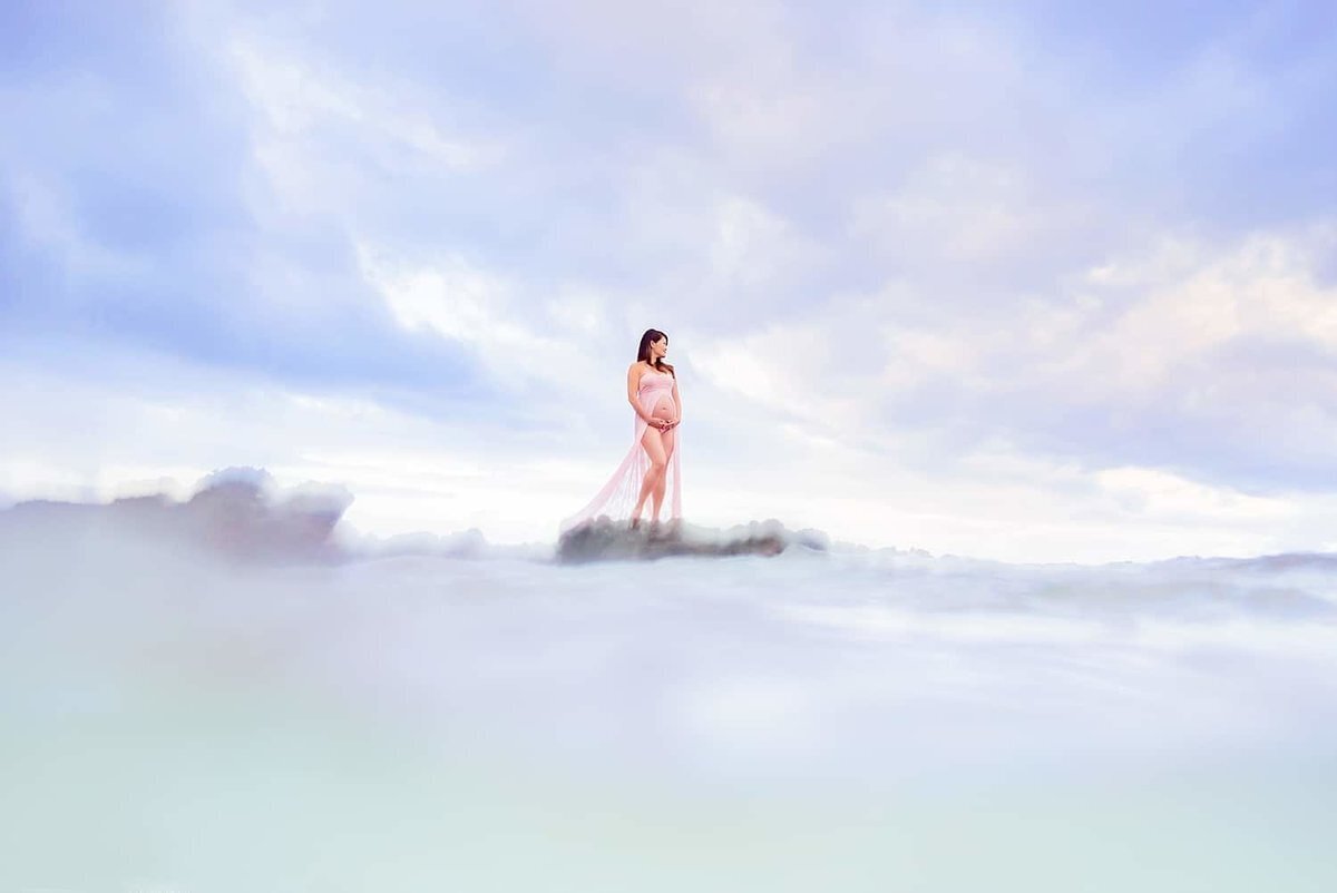 Unique maternity portrait feautring woman with pink pregnancy gown standing on lava rock in Wailea for her session with Love + Water Photography