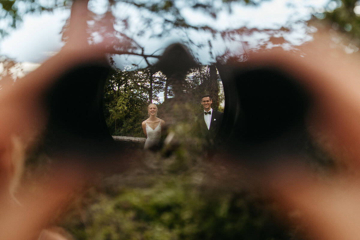 View through binoculars of bride sitting in garden