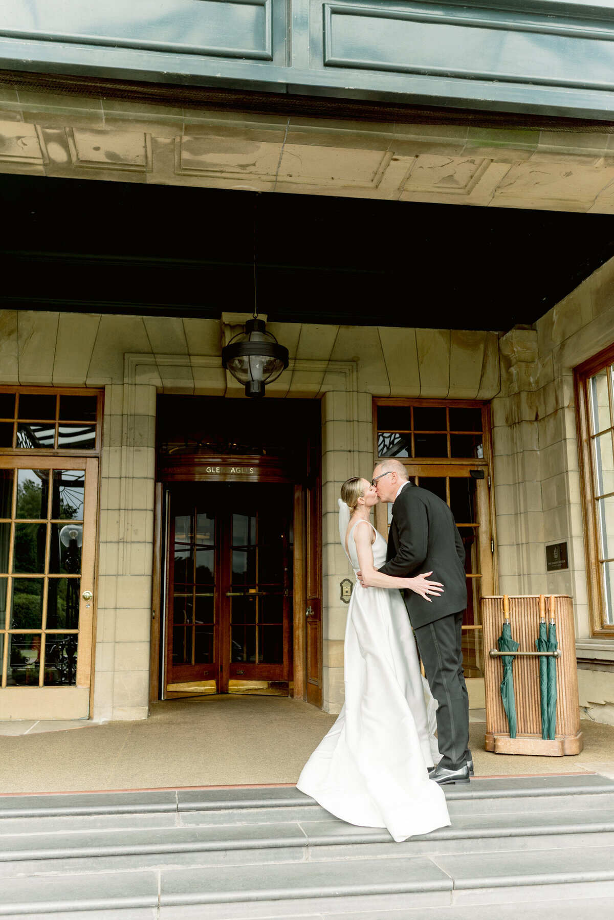 Editorial wedding photograph of Bride and Groom kissing in front of Gleneagles hotel on their wedding day. Image by award winning luxury wedding photographer Scotland, Jill Cherry Porter.