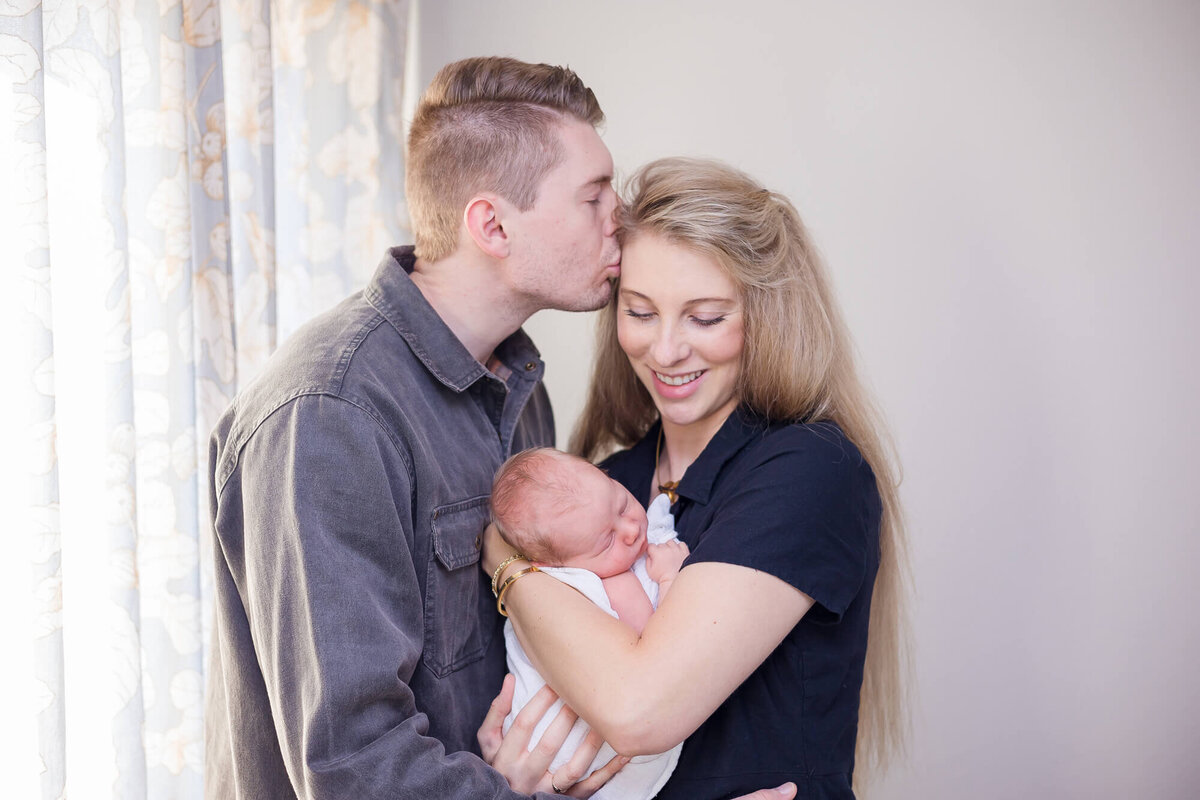 Happy mom holding her newborn son with husband kissing her on the temple