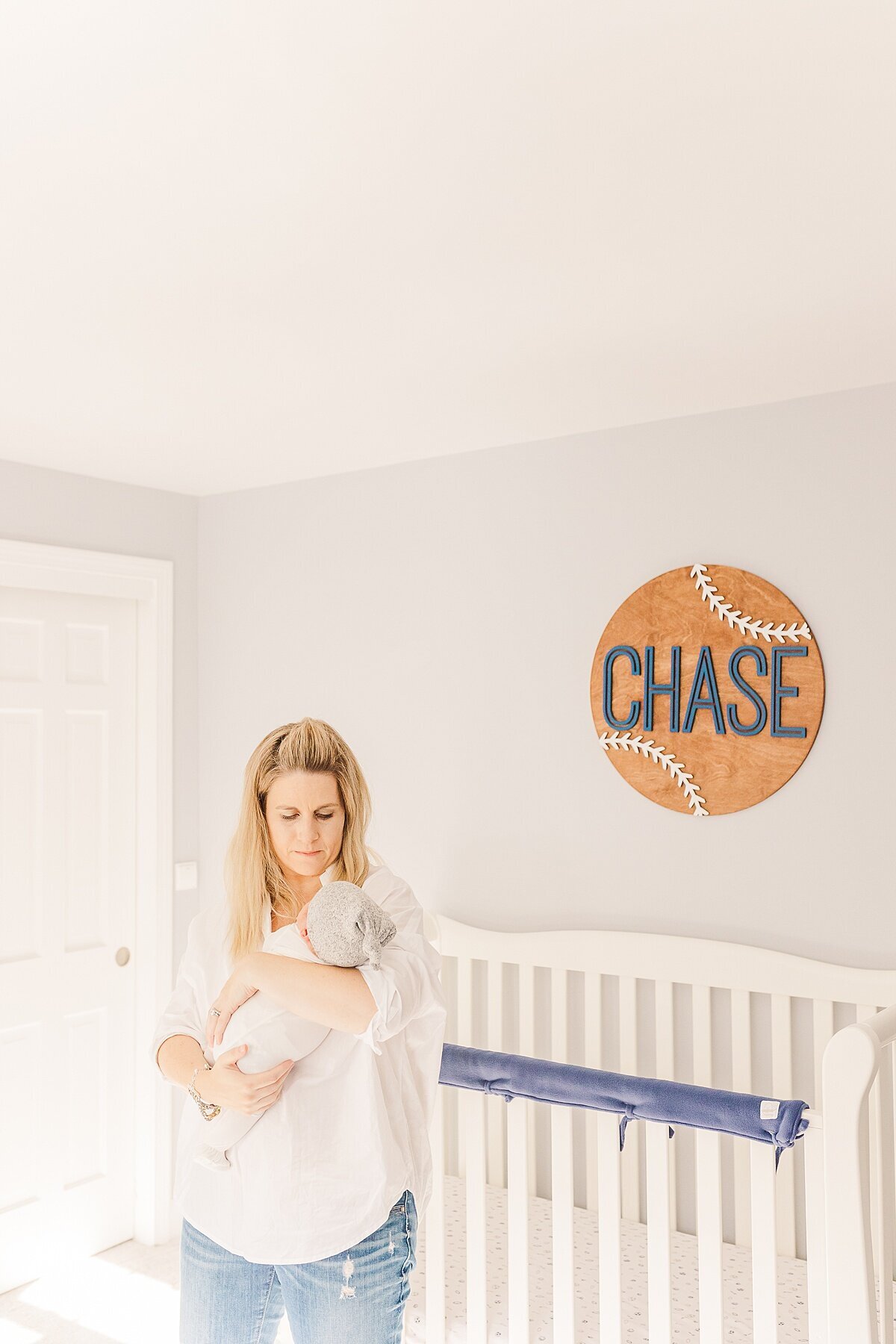 mom holds baby next to crib  during in home newborn photo session with Sara Sniderman Photography in Sherborn Massachusetts