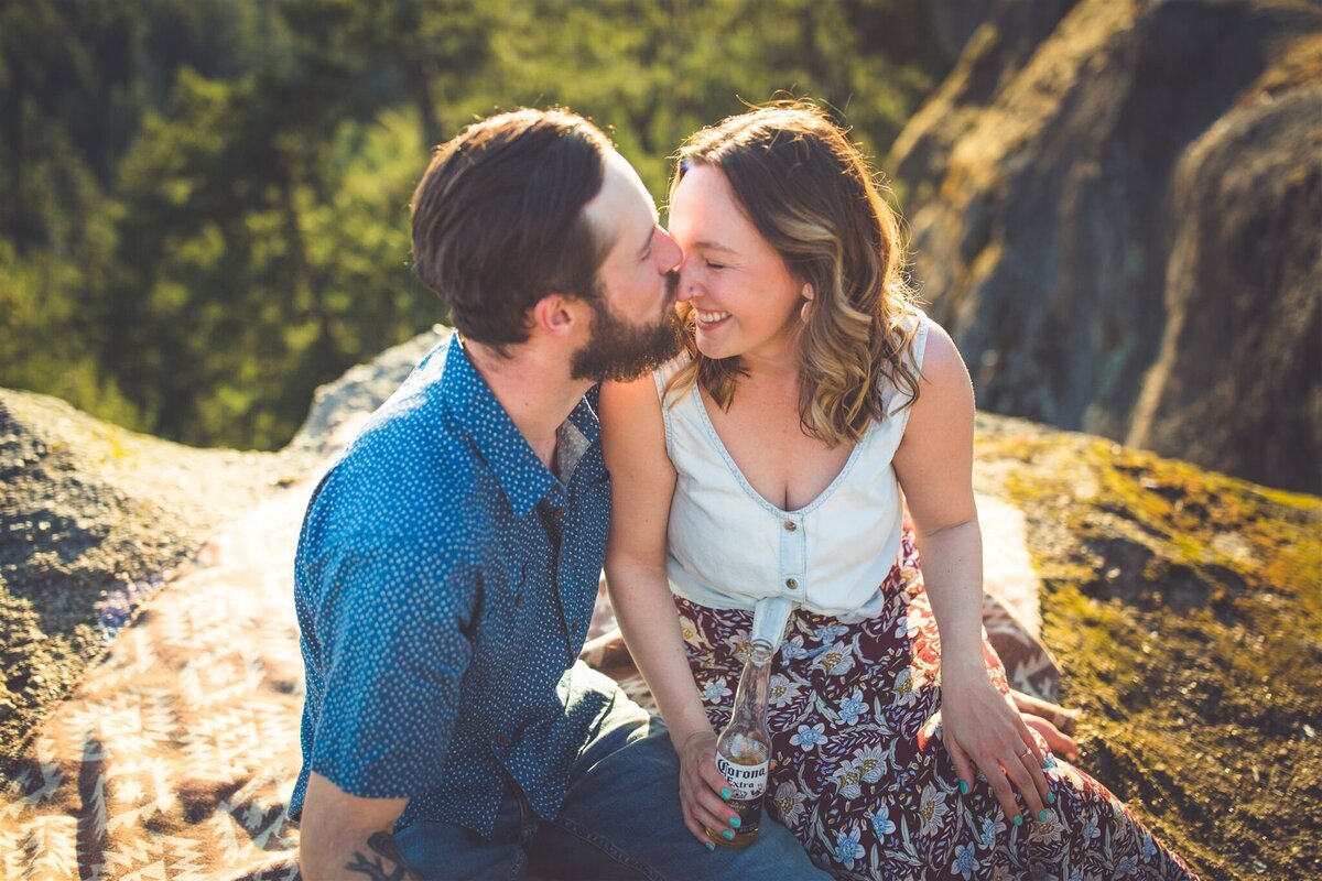 A couple smiling and kissing on rock in Vancouver Island during their engagement photo session.