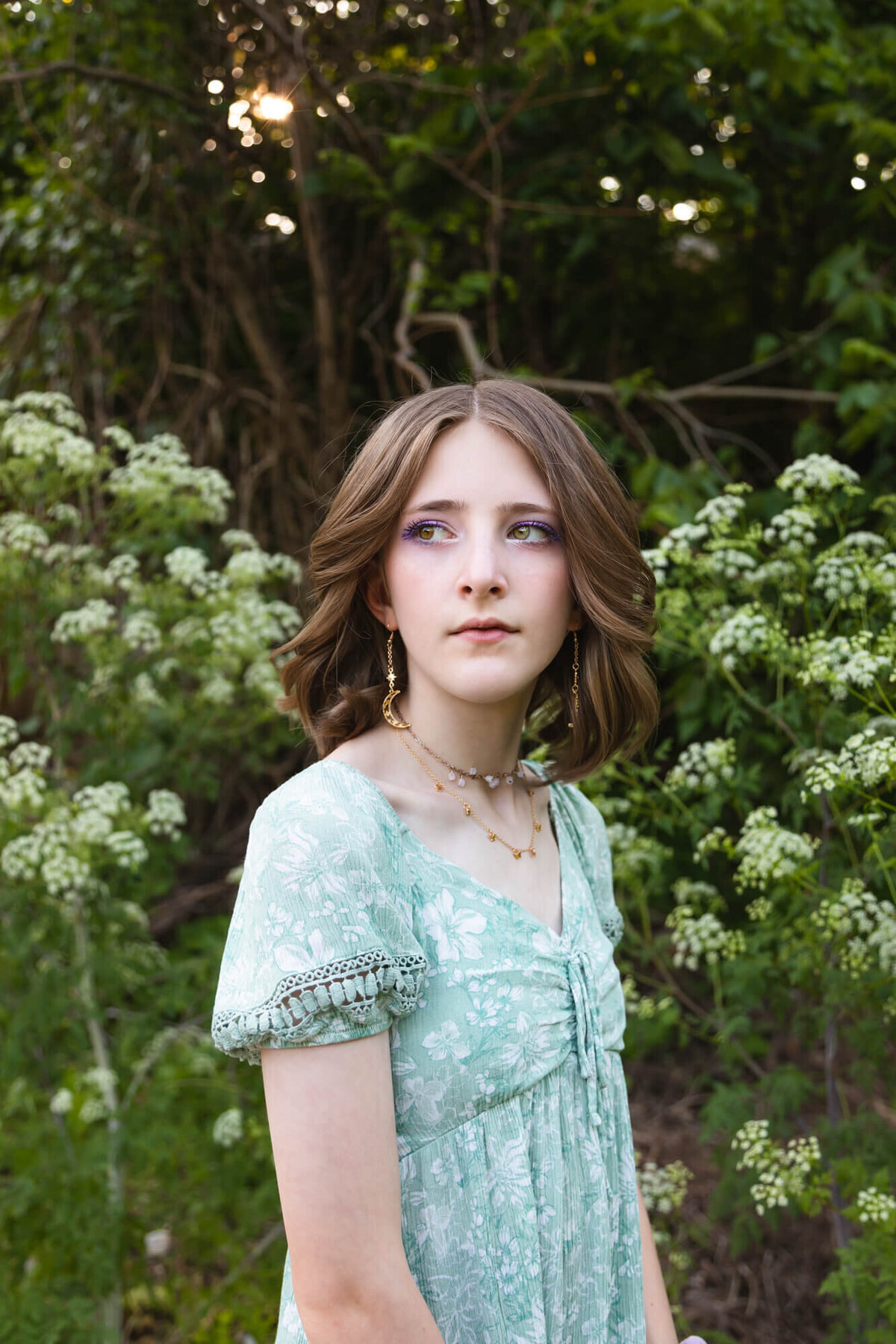 Lovely young teen girl in a floral green dress looking off to her right posing in front of white wildflowers. Captured by Springfield, MO teen photographer Dynae Levingston.
