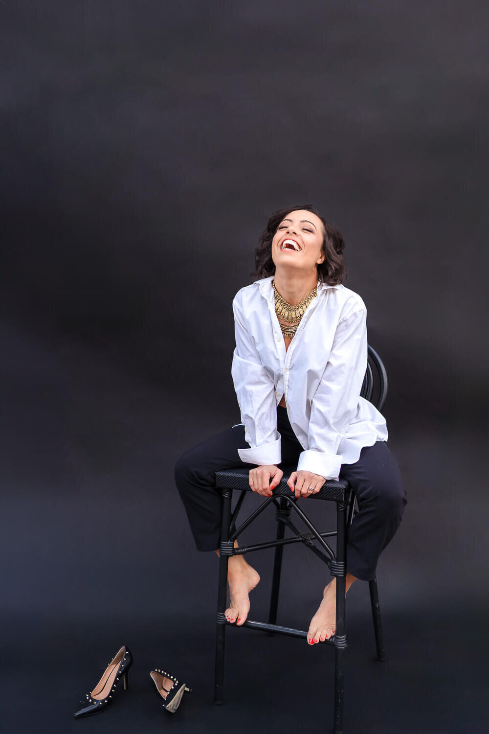 creative portrait of woman laughing on stool with head back 