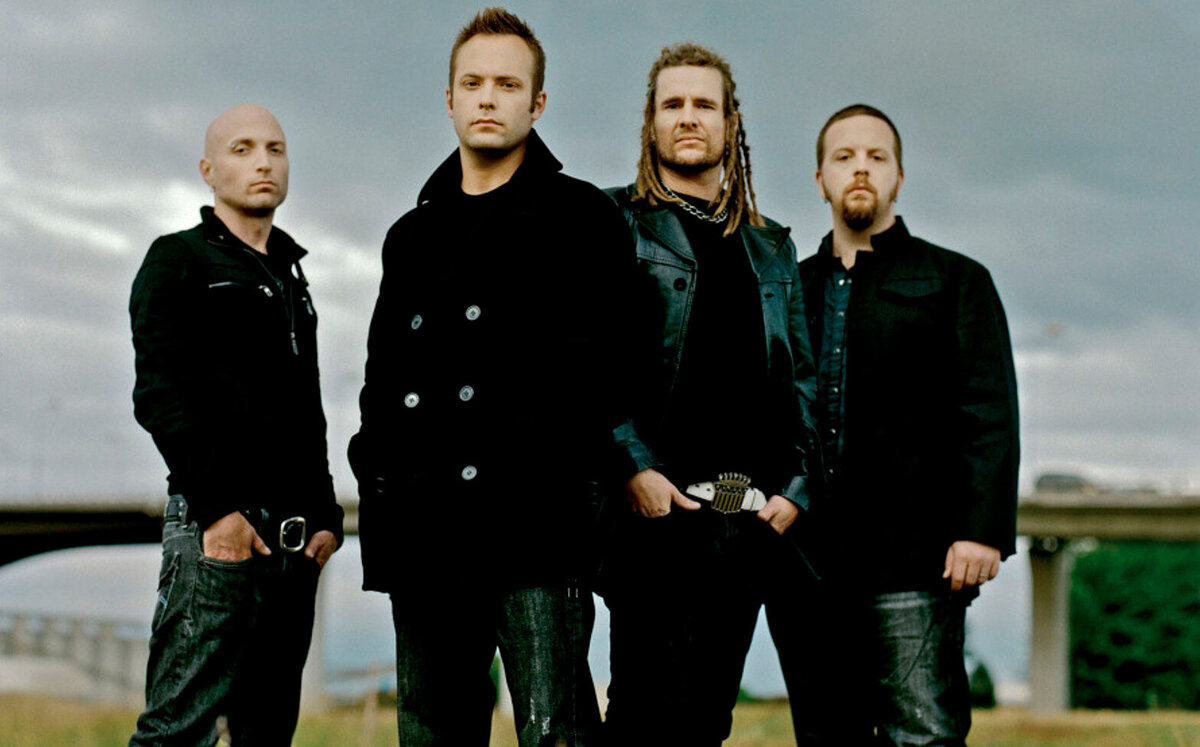 Photo of band Default all four members standing in grass with bridge behind them
