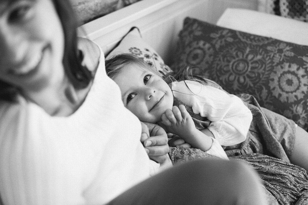 Young child lying next to a parent and smiling, a candid family photoshoot in Sydney