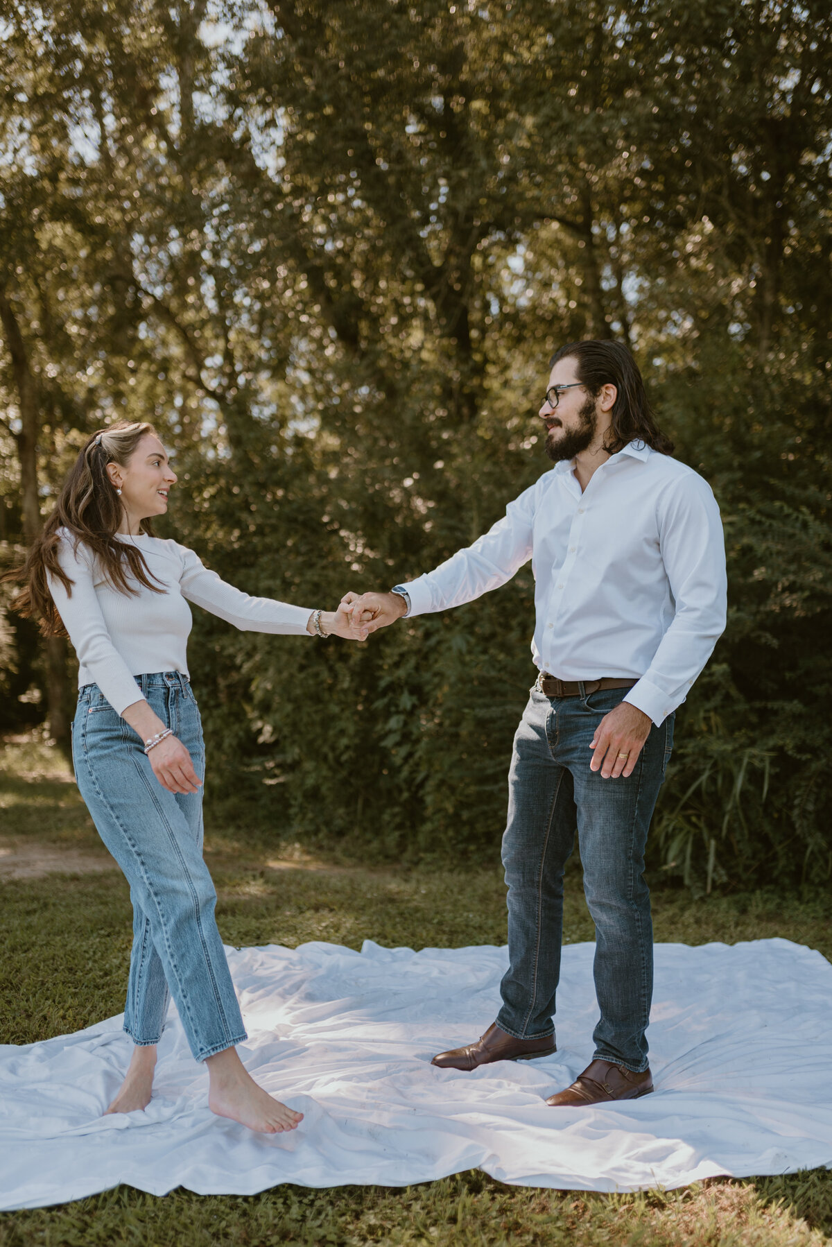 a couple holding hands while standing on a white sheet in the grass.