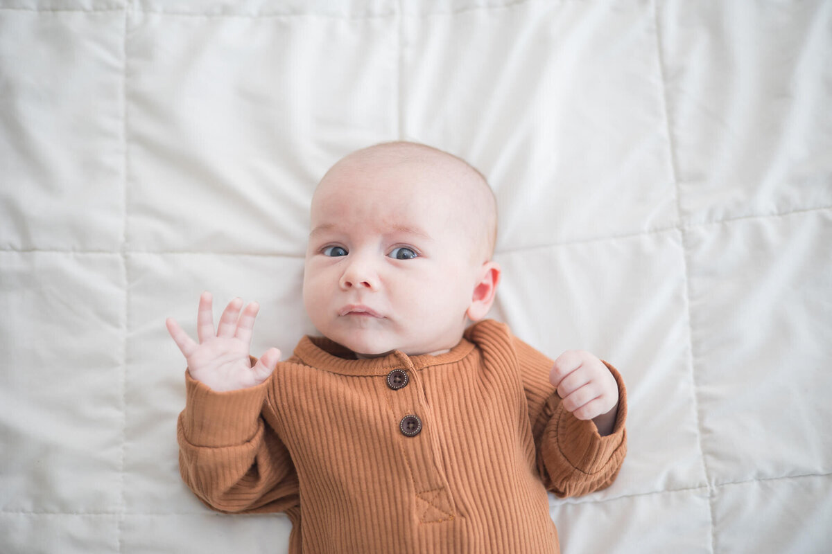 concerened and shocked look on newborn baby boys face as he lays on a bed