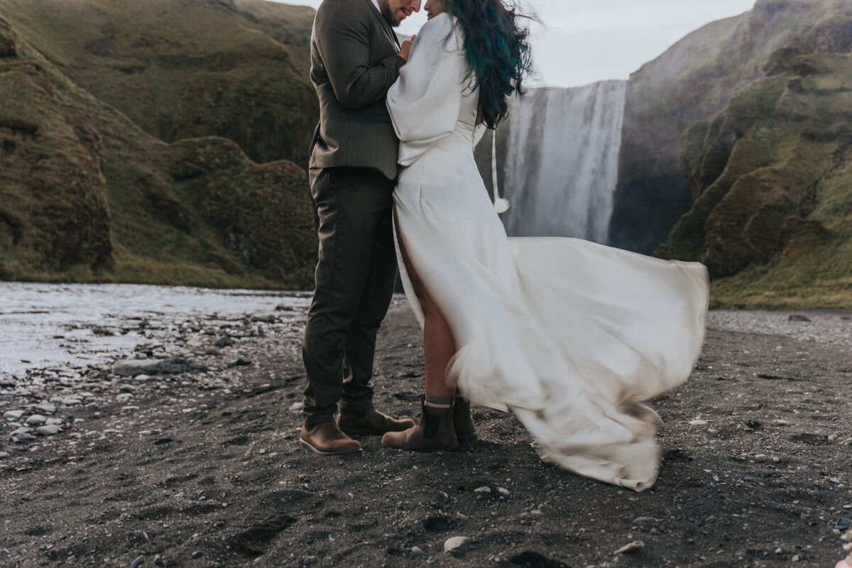 A husband and wife kiss under the mist of a secluded waterfall