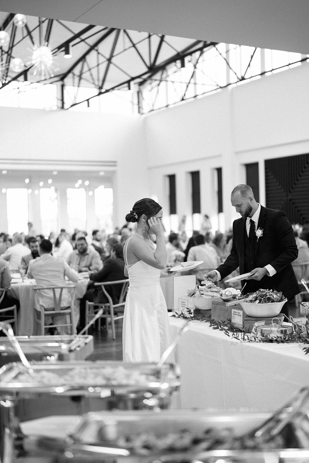 Black and white candid photo of the bride and groom putting food on their plates during their Leona Road wedding reception dinner.
