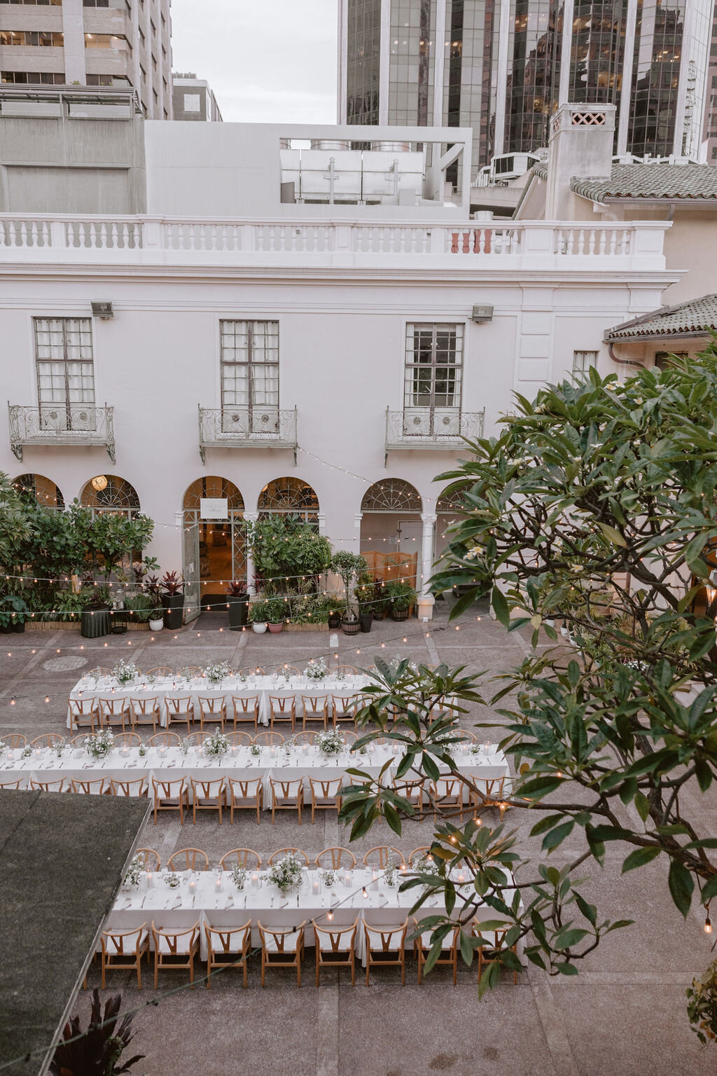 overhead view of three wedding reception tables that are very long and lined up with ivory tableclothes surrounded by buildings