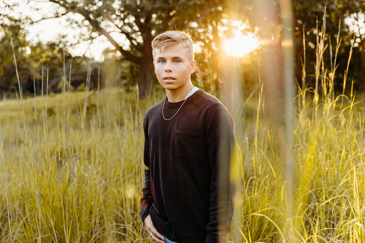 high school senior boy in a black shirt standing in a  grassy field