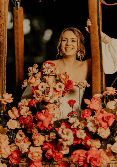 Mariée, souriante, posant dans une montgolfière garnie de fleurs corails et rose pastel lors d'une séance photo mariage.