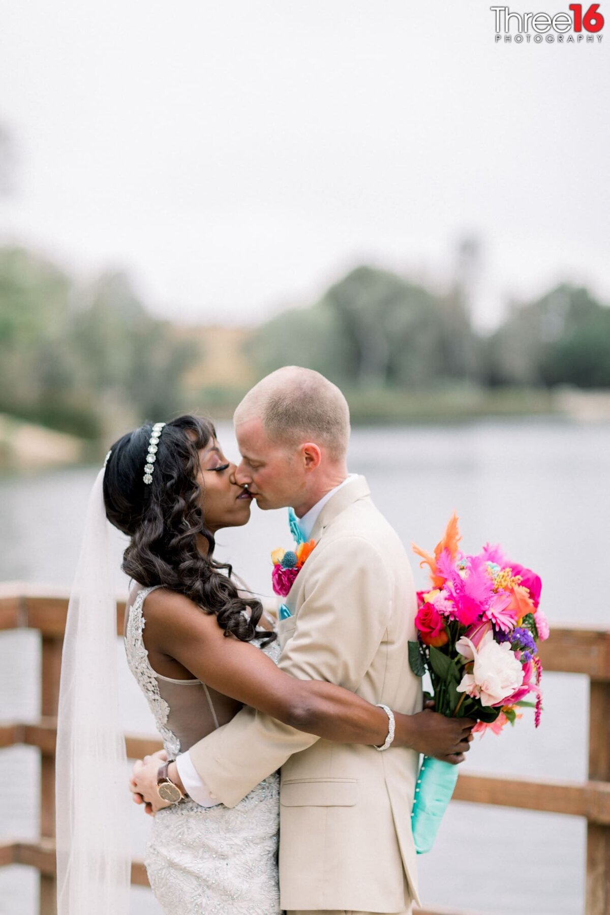 Bride and Groom fully embrace each other while sharing a kiss on a dock overlooking a small lake