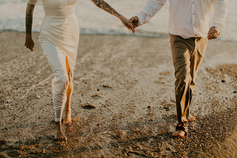 Couple marchant sur la plage et se tenant par la main dans une lumière douce et naturelle capturée par Laura, photographe couple en vendée.