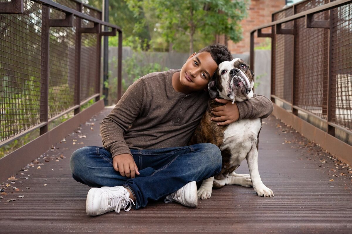 portrait of a boy wearing brown holding his brown and white drooling dog