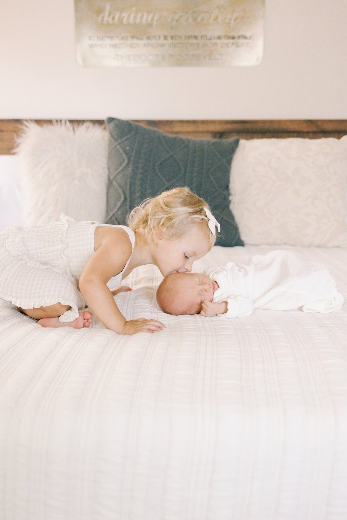 Big sister kissing newborn baby brothers head while laying on bed in Williamsburg Virginia