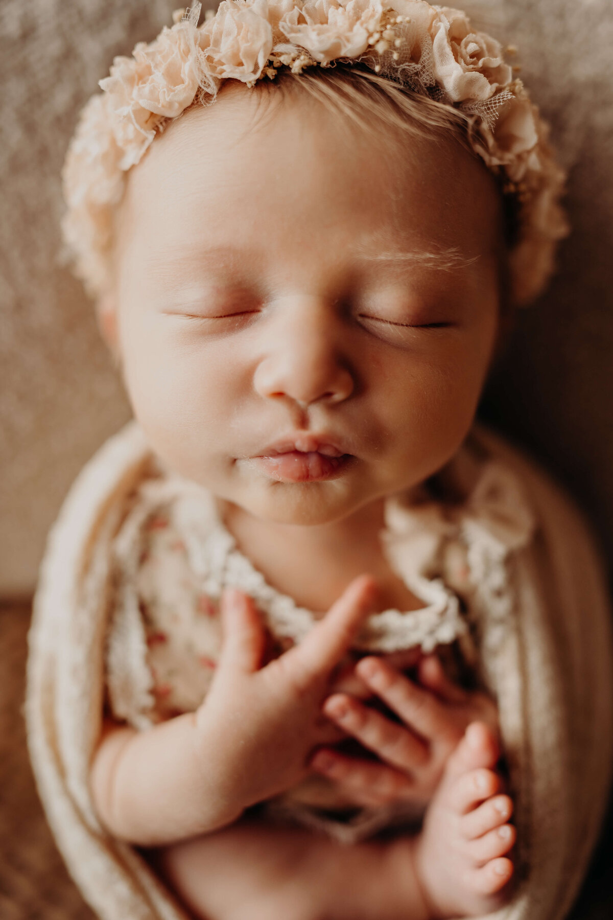 iconic newborn baby girl puckering lips while swaddled wearing a flower crown