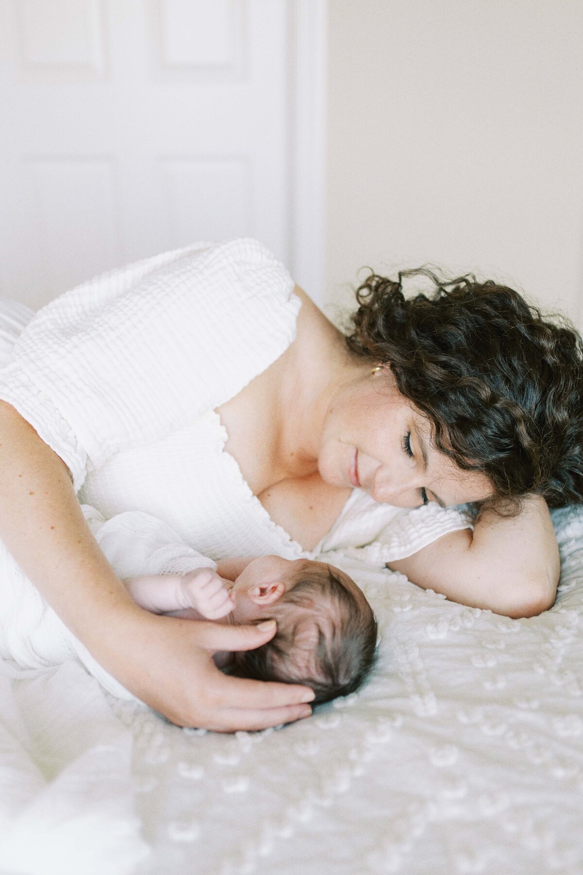 mom snuggling newborn baby on bed