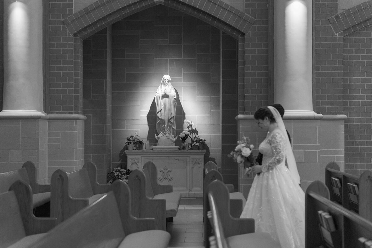 A couple walks by a statue of the Blessed Mother Mary during their Catholic wedding.