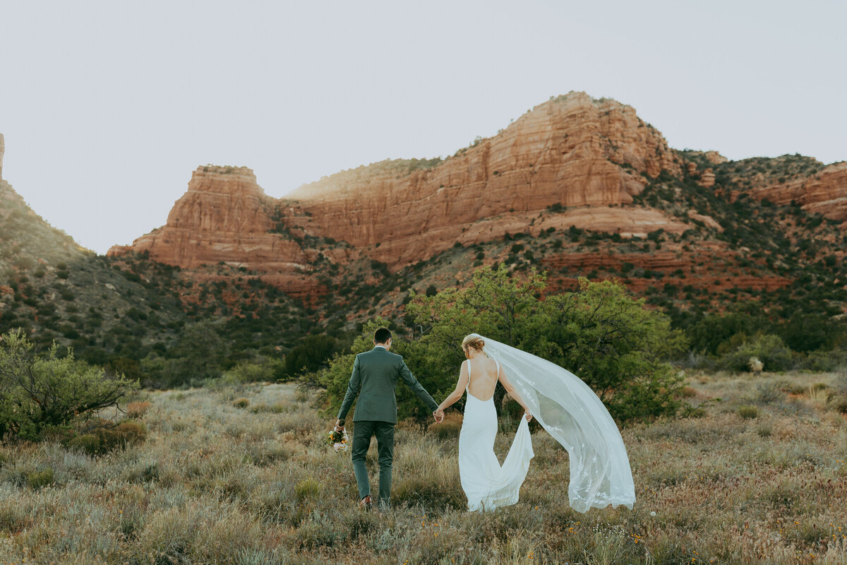 groom and bride walk together with red rock views around them in sedona