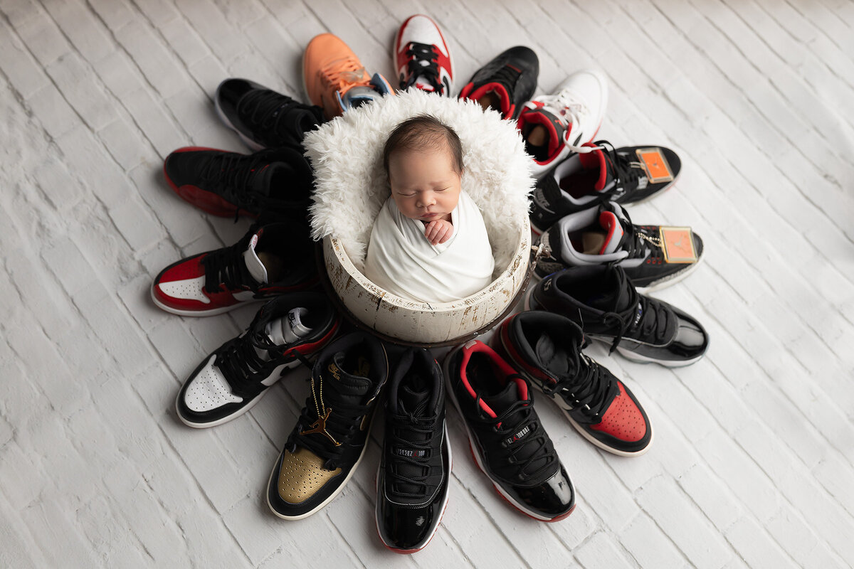 Newborn wrapped in white surrounded by a full collection of Air Jordans, captured in a creative sneaker-themed setup by Dallas newborn photographer.