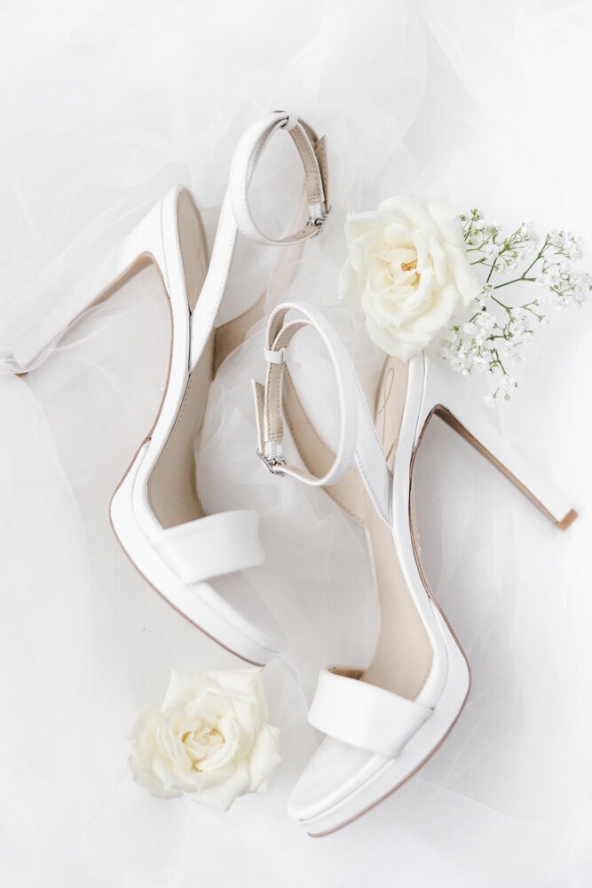 flat lay of white bridal shoes with flowers