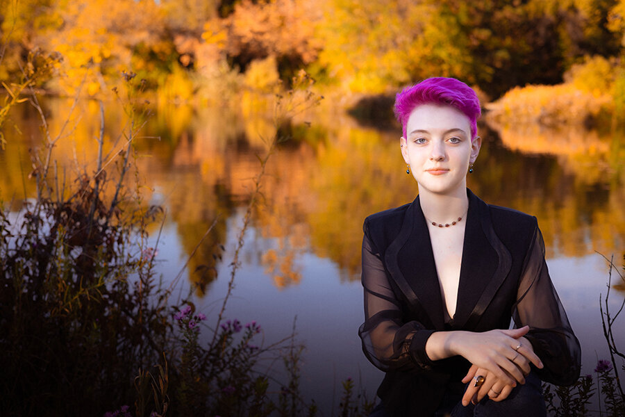 High school senior sitting at a reflective pond in fall.