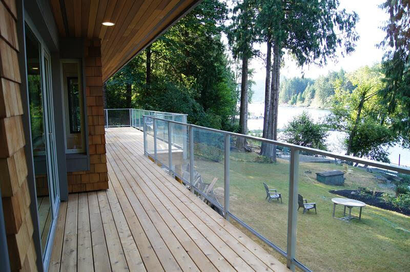 Lake house patio design with steel and glass railings surrounding wood deck.