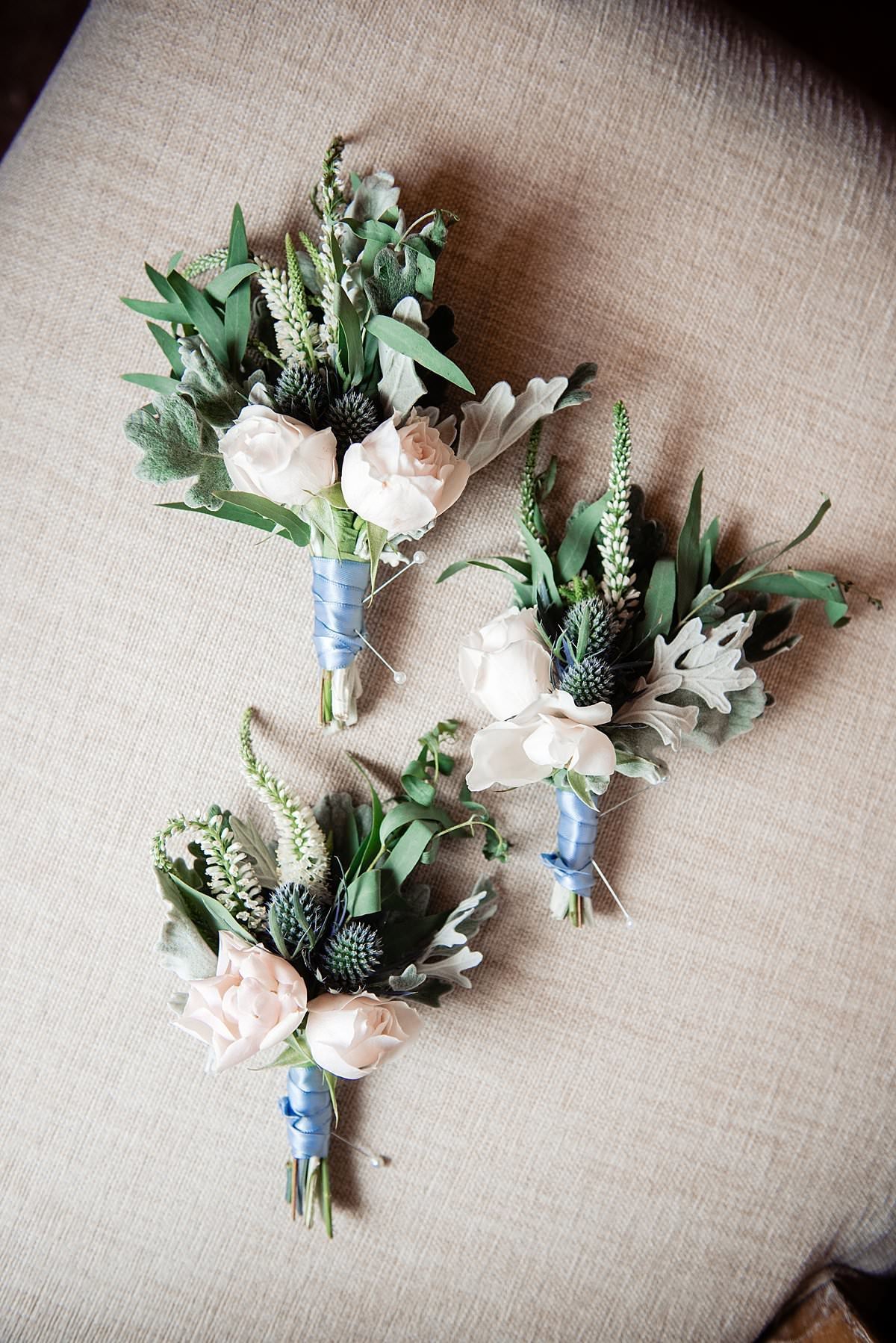 Boutonnieres of ivory mini roses with greenery sprigs
