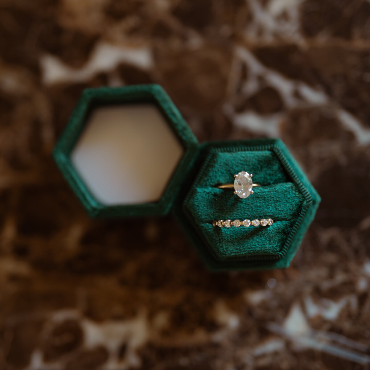 Close-up of a diamond engagement ring and wedding band displayed in a green velvet hexagonal box, captured on a marble surface during a DFW wedding. The image highlights the elegance and detail of the bridal jewelry.