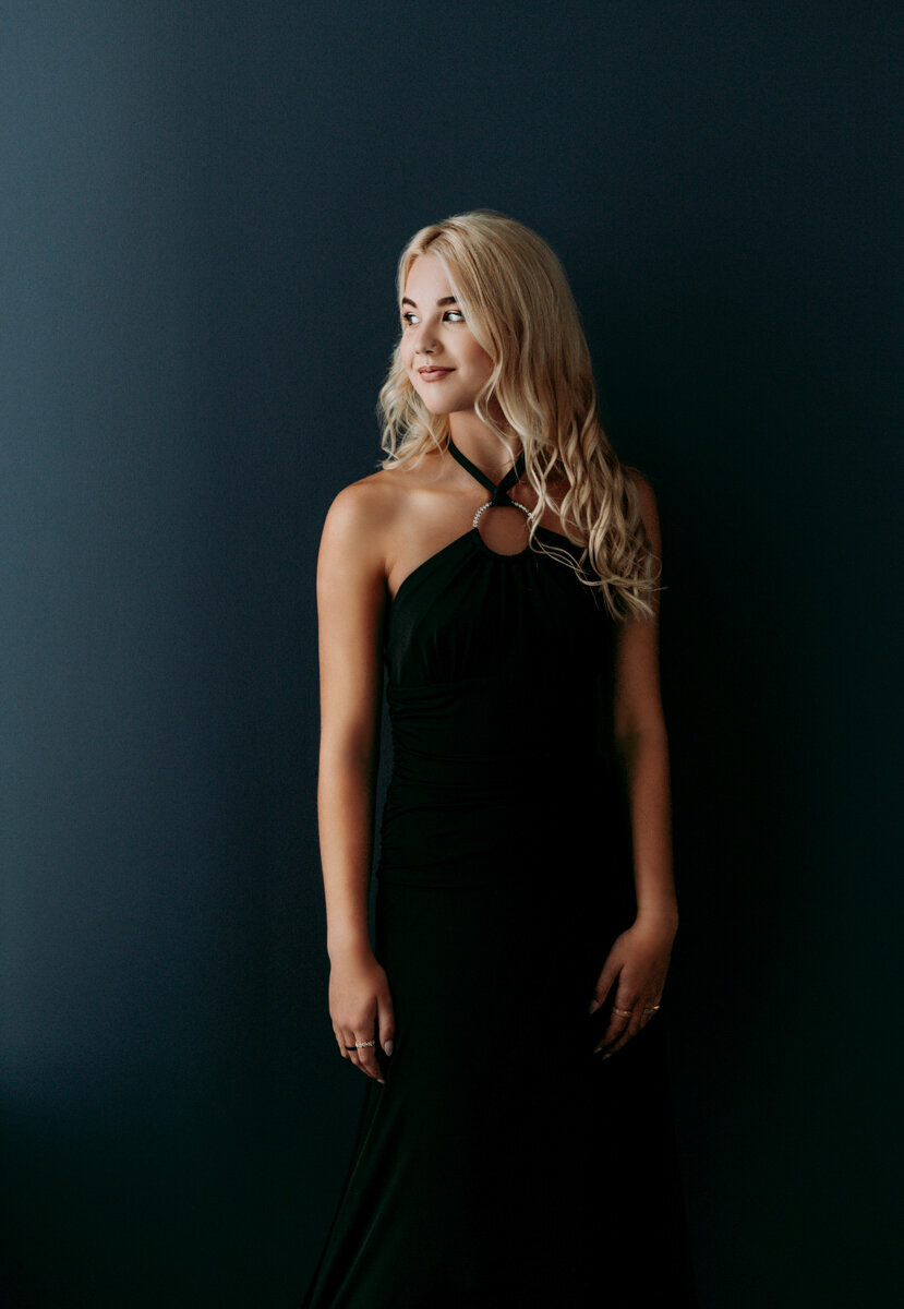 Soft-lit studio portrait of a senior girl in a black gown, exuding elegance and poise.