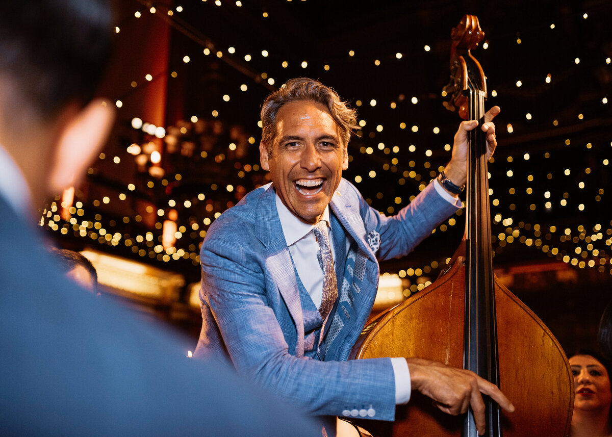 A smiling man plays the double bass under a canopy of fair lights at a wedding design by a london wedding planner.